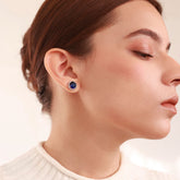 Close up of Azuline Halo platinum-plated stud earrings with a dark blue centerpiece and radiant halo accents